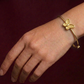 Gold bracelet with butterfly design on a wrist against a dark background