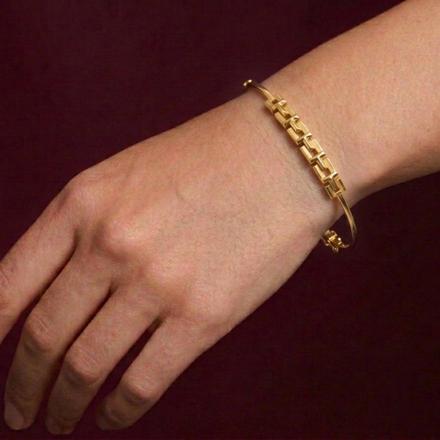Gold bracelet on a wrist against a dark red background