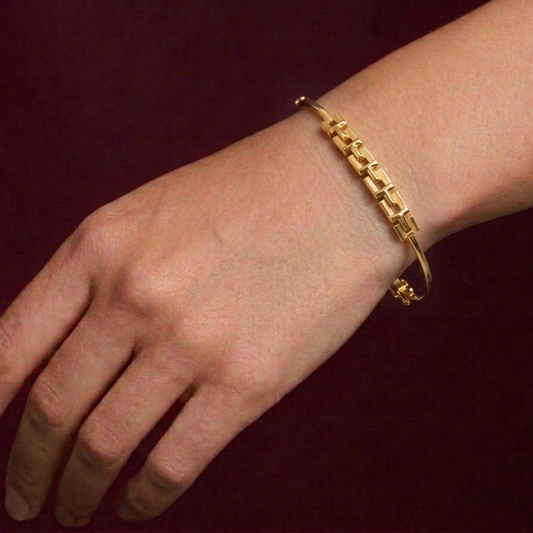 Gold bracelet on a wrist against a dark red background