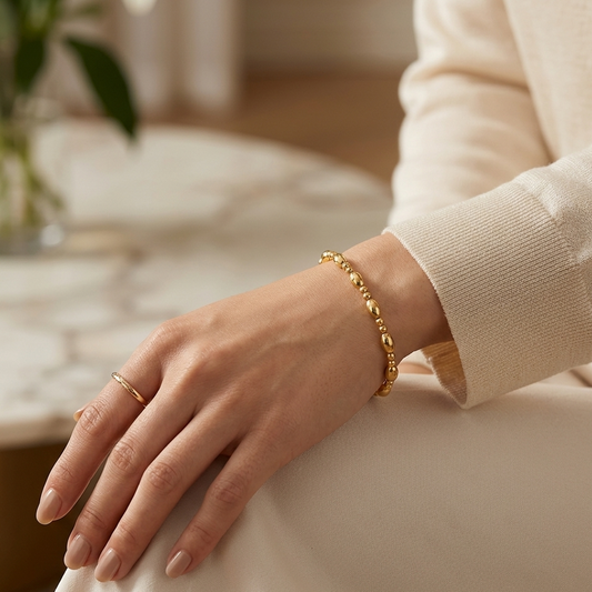 Hand wearing a gold bracelet on a neutral background