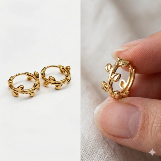 Gold hoop earrings with leaf designs held by a hand against a neutral background