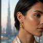 Close-up of a woman wearing gold hoop earrings with a blurred cityscape background