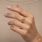 Hand wearing a gold heart-shaped ring on a beige background