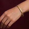 Gold bracelet on a wrist against a dark background