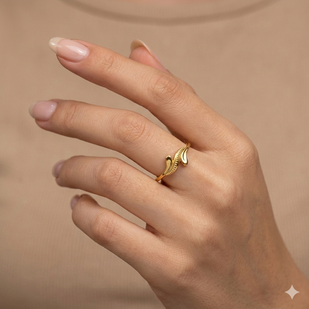 Gold ring with leaf design on a hand against a beige background