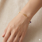 Gold bracelet with a purple bead on a hand against a beige background
