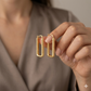 Gold hoop earrings held by a hand against a neutral background
