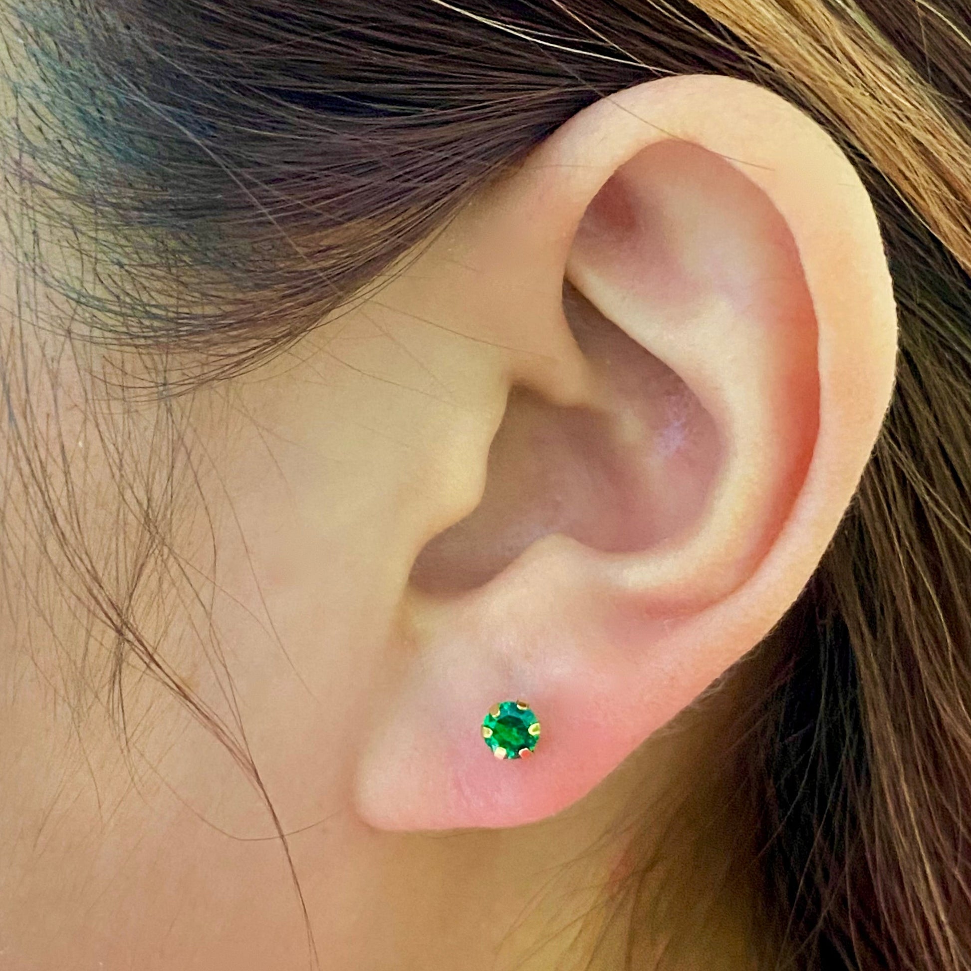 Green gemstone stud earring in gold setting on ear, close-up jewelry photo