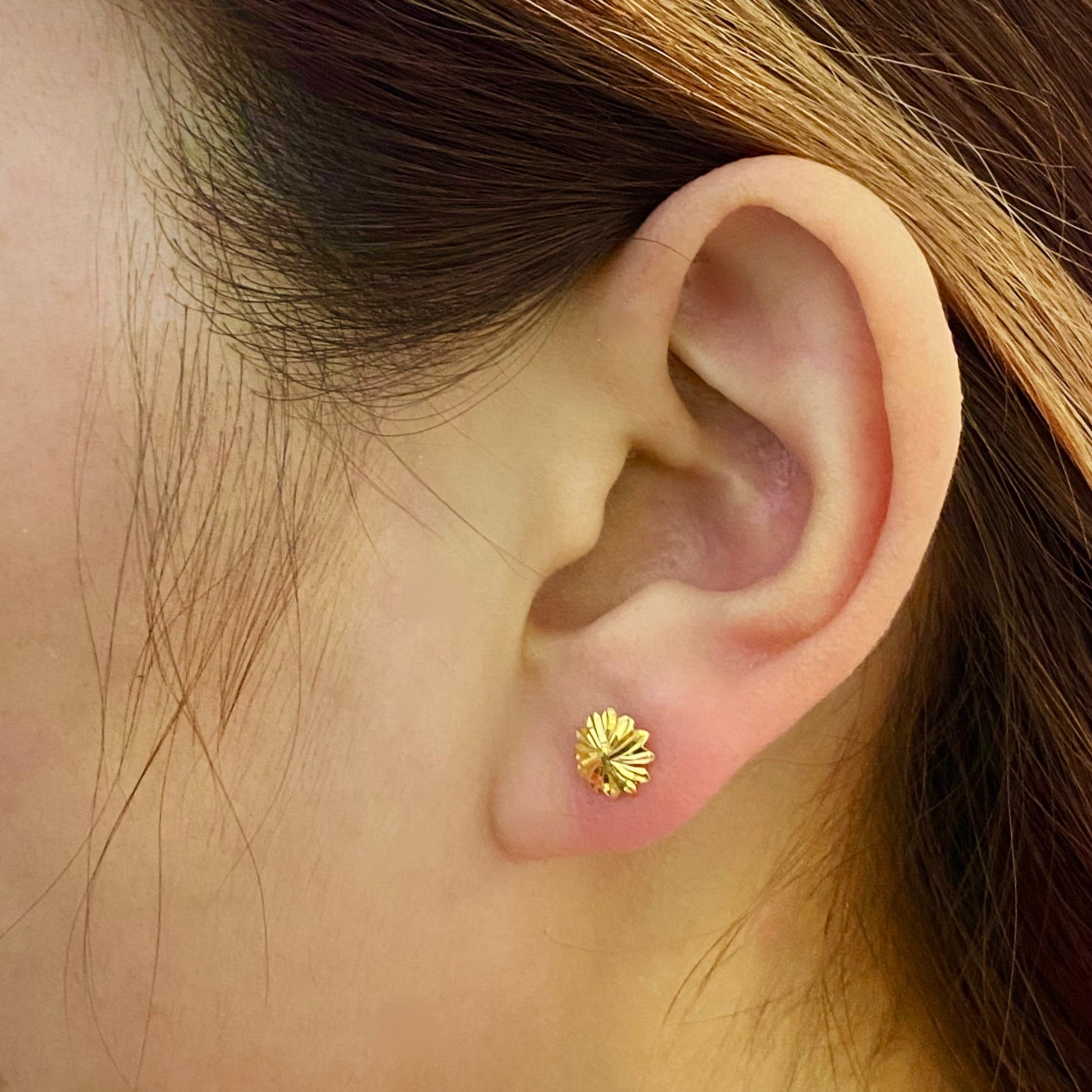 Woman wearing gold flower stud earring, close-up on ear, elegant gold jewelry