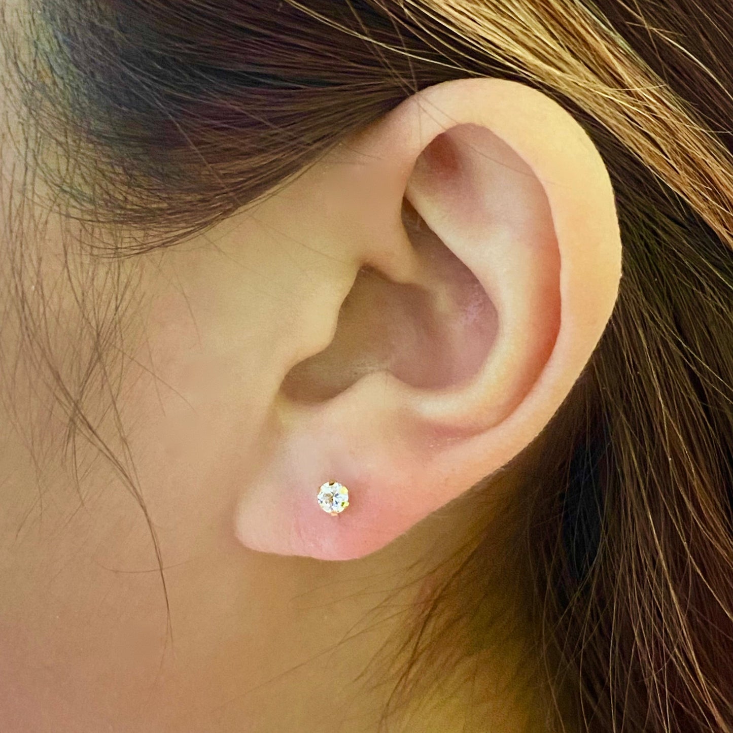 Close-up of a woman's ear wearing a round diamond stud gold earring
