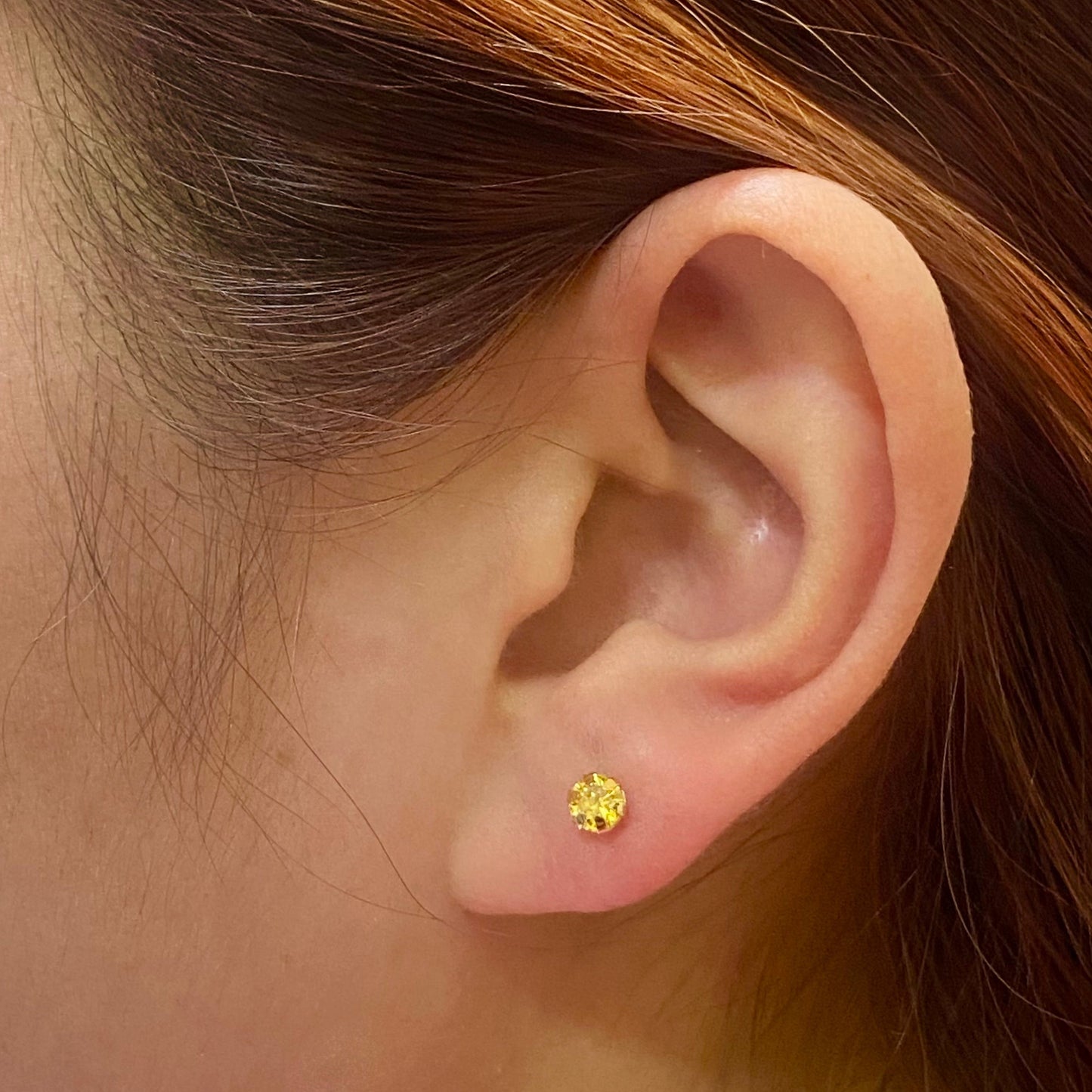 Close-up of ear wearing a round yellow gold stud earring