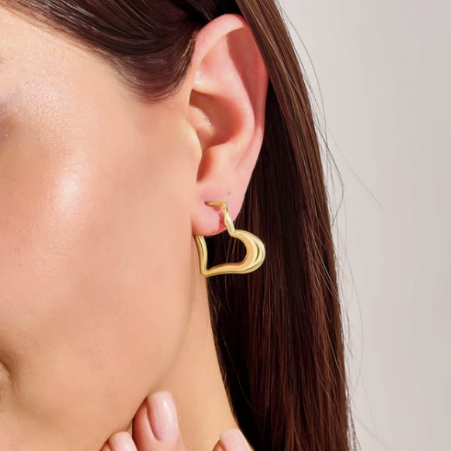 Close-up of a person wearing a gold heart-shaped earring against a neutral background