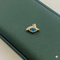 Gold eye-shaped brooch with blue gemstone on a green leather surface