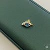 Gold eye-shaped brooch with blue gemstone on a green leather surface