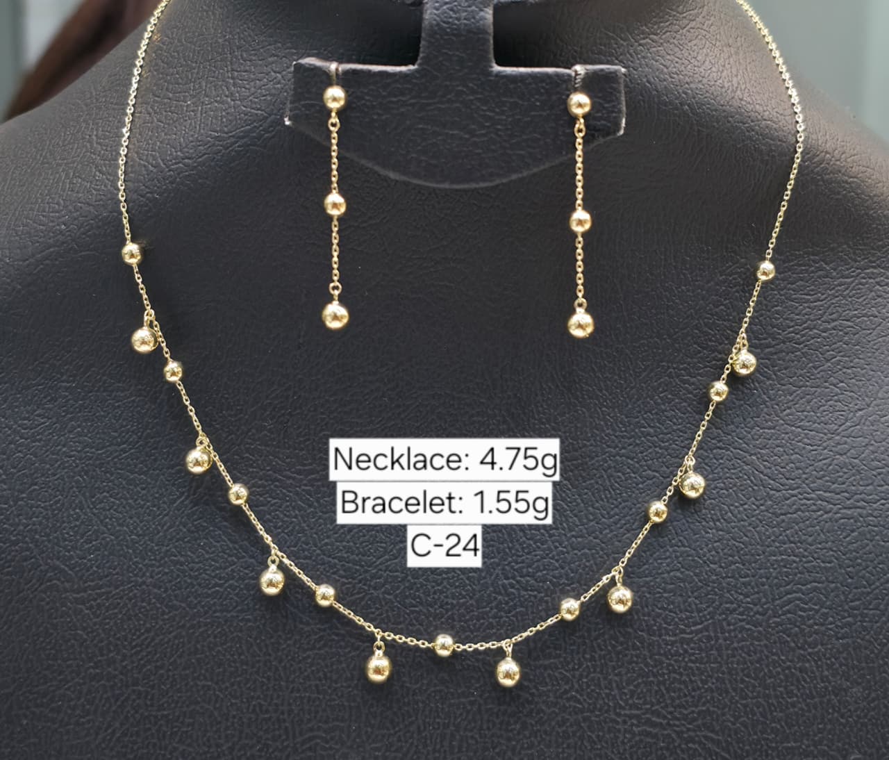 Gold necklace and earrings on a black stand with weight labels.