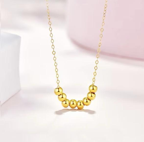 Gold necklace with round beads on a light pink background