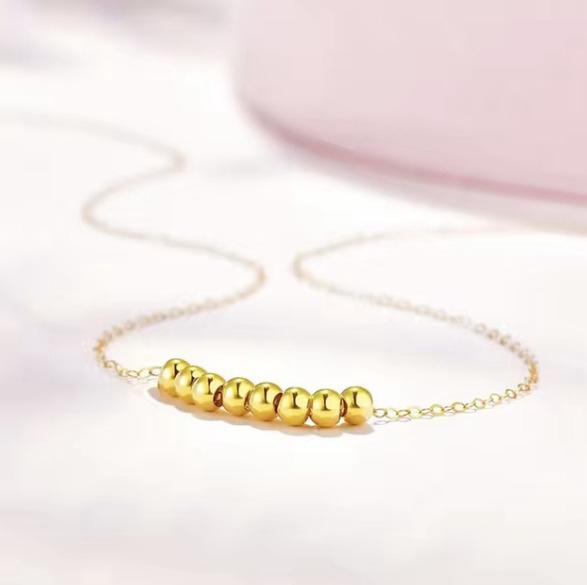 Gold necklace with round beads on a light pink background