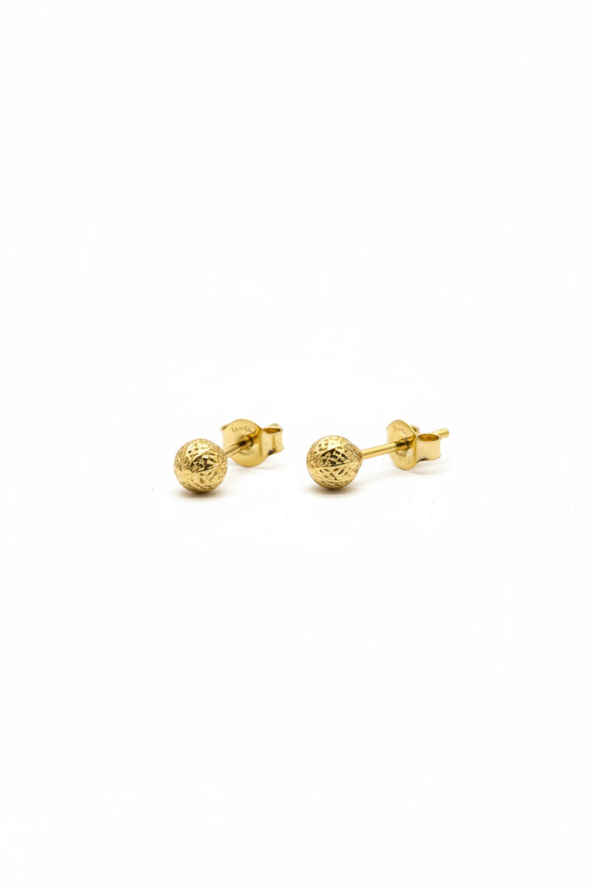 Gold earring on a digital scale with a wooden surface and white towel in the background