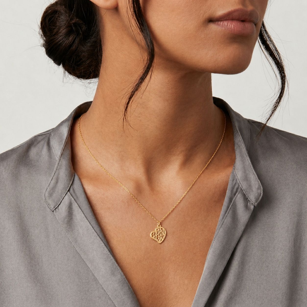Woman wearing a gold necklace with a heart pendant on a plain background