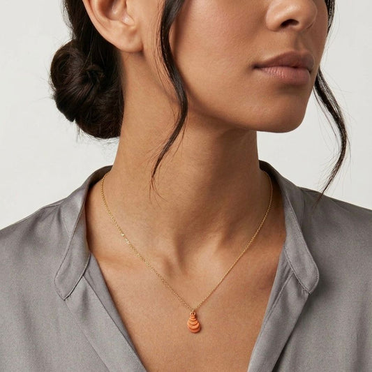 Close-up of a woman wearing a gold necklace with a pendant against a neutral background