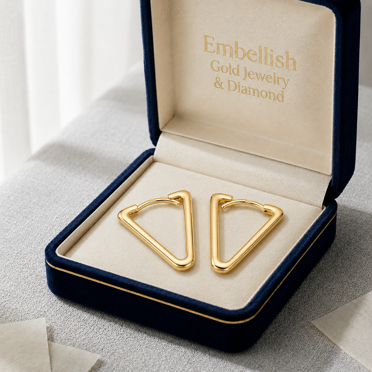 Gold earrings in a 'Embellish Gold Jewelry & Diamond' box on a light background