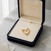 Gold heart-shaped jewelry in an open 'Embellish Gold Jewelry & Diamond' box on a textured surface.