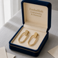 Gold earrings in a 'Embellish Gold Jewelry & Diamond' box on a textured surface.