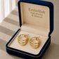 Gold hoop earrings in a 'Embellish Gold Jewelry & Diamond' box on a textured surface.