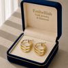 Gold hoop earrings in a 'Embellish Gold Jewelry & Diamond' box on a textured surface.
