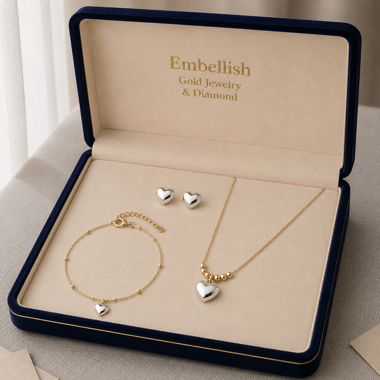 Gold jewelry set with heart-shaped charms in an 'Embellish' jewelry box.