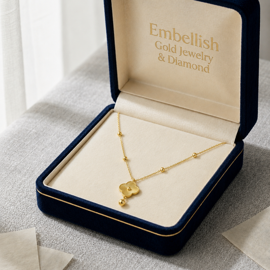 Gold necklace with clover pendant in an open jewelry box labeled 'Embellish Gold Jewelry & Diamond'.