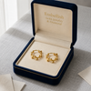 Gold earrings in a 'Embellish Gold Jewelry & Diamond' box on a textured surface