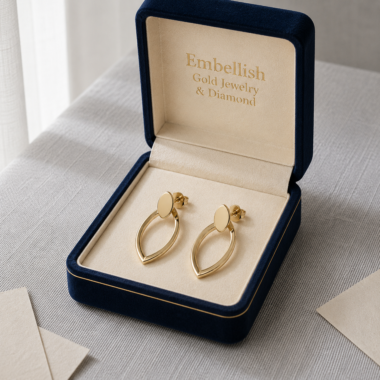 Gold earrings in a 'Embellish Gold Jewelry & Diamond' box on a light surface.