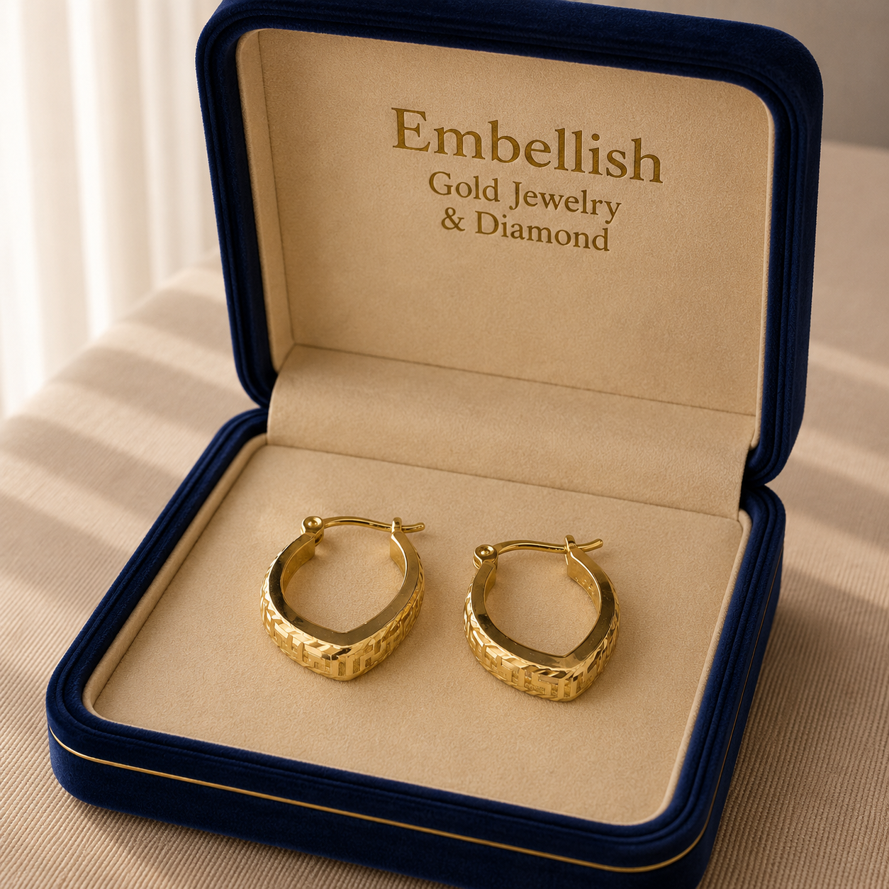 Gold hoop earrings in a 'Embellish Gold Jewelry & Diamond' box on a beige surface.