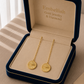 Gold earrings in an open jewelry box with 'Embellish' branding.
