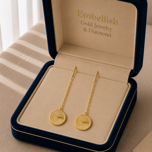 Gold earrings in an open jewelry box with 'Embellish' branding.